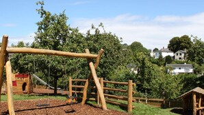 Une aire de jeux avec des structures en bois, une balançoire et une petite maison de jeu.
