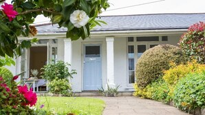 Une maison avec un porche à l’avant, une pelouse et diverses plantes et fleurs.