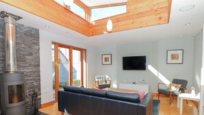Un salon moderne avec un grand canapé en cuir noir, un plafond en bois, une cheminée en pierre et un téléviseur fixé au mur.