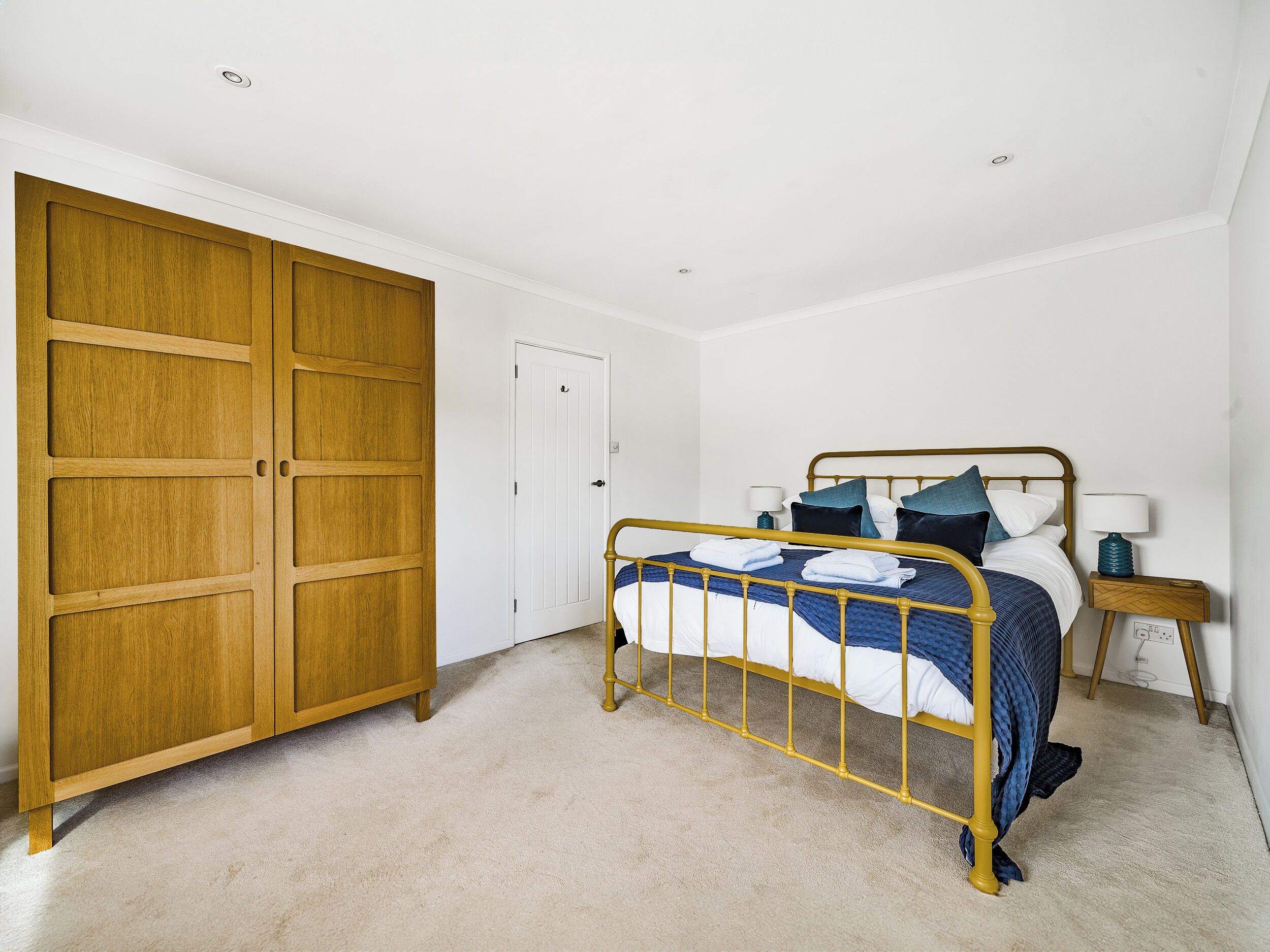 A bedroom with a large wardrobe, a bed with a metal frame, and a bedside table with a lamp.