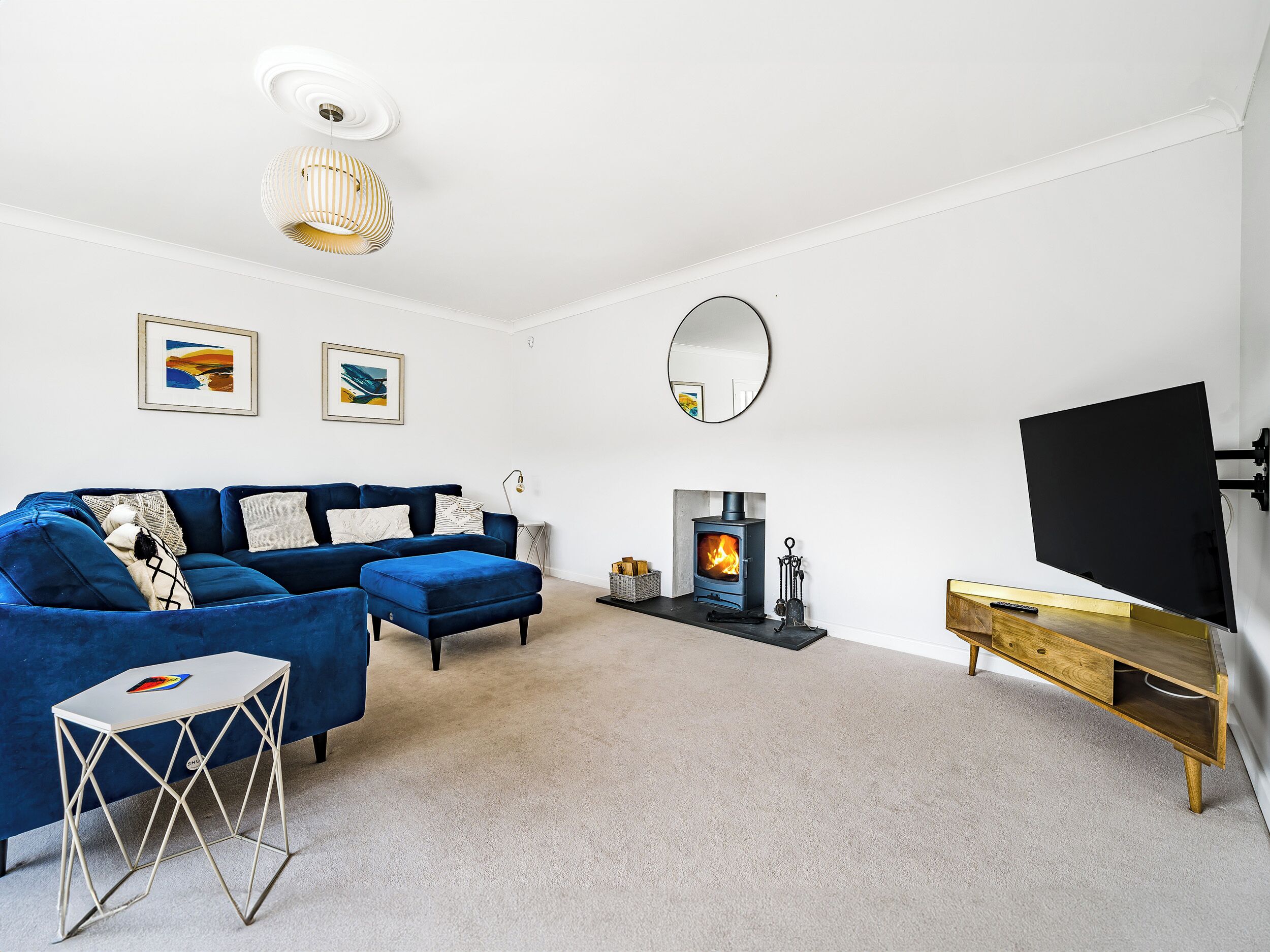 A modern living room with a blue sofa, a small white table, a TV, a fireplace, and a mirror on the wall.
