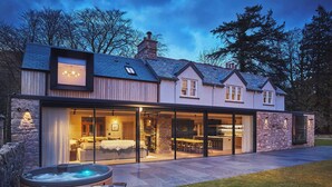 A modern house with a large glass door leading to a dining area and a bedroom. There are two hot tubs in the foreground. - Eskdale Retreat (Holmrook)
