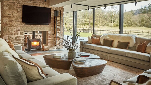 A modern living room with a stone fireplace, a large flat-screen TV, and a sofa facing a scenic outdoor view. - Eskdale Retreat (Holmrook)