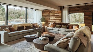 A modern living room with a large sectional sofa, two round coffee tables, and a stone wall. - Eskdale Retreat (Holmrook)