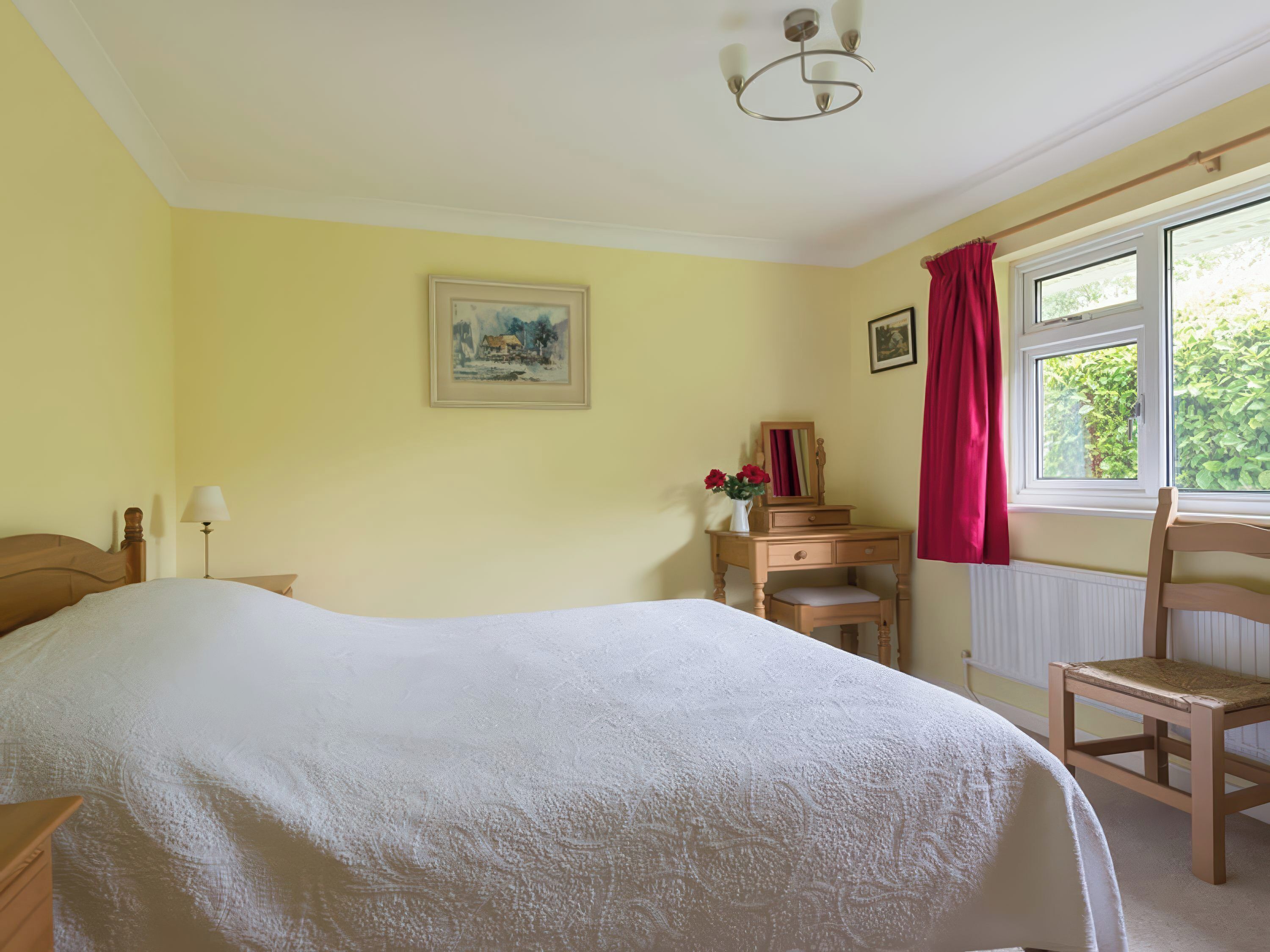 A bedroom with a bed, a dresser, a chair, a window with curtains, and a painting on the wall.