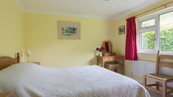 A bedroom with a bed, a dresser, a chair, a window with curtains, and a painting on the wall.