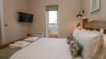 A hotel room with a bed, a flat-screen TV mounted on the wall, a window with a view of trees, and a bedside lamp.