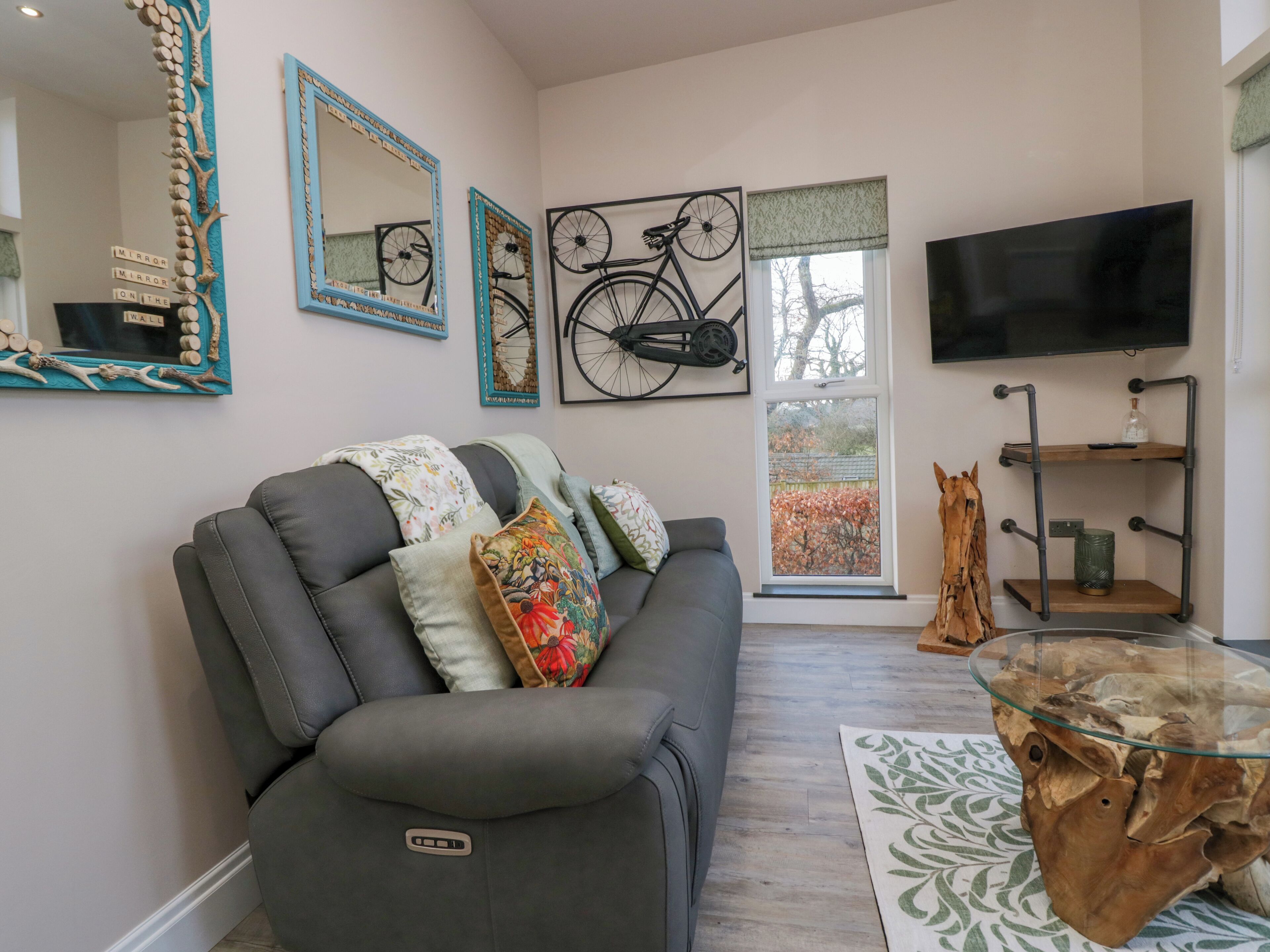 Un salon avec un canapé gris, des coussins décoratifs, un téléviseur fixé au mur et des œuvres d’art accrochées aux murs.
