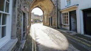 Eine enge Gasse mit einem steinernen Torbogen, Steinhäusern und einem in der Ferne geparkten Auto.