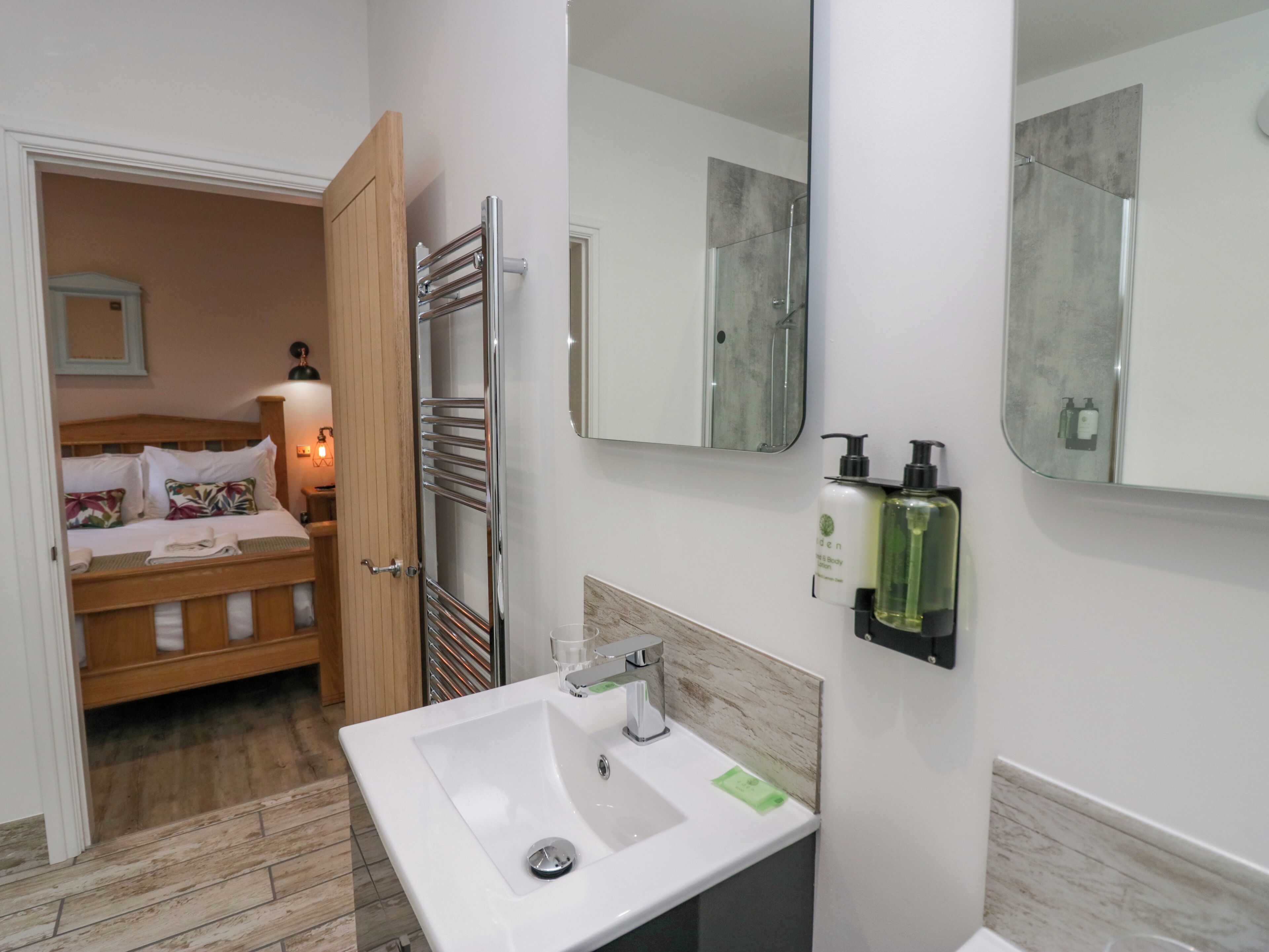 Habitació d'hotel amb un llit de fusta, un lavabo blanc i un mirall gran.