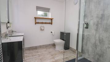 Une salle de bain moderne avec une douche à parois de verre, des toilettes blanches et une étagère en bois au-dessus du lavabo.