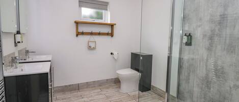 A modern bathroom with a glass shower enclosure, a white toilet, and a wooden shelf above the sink.