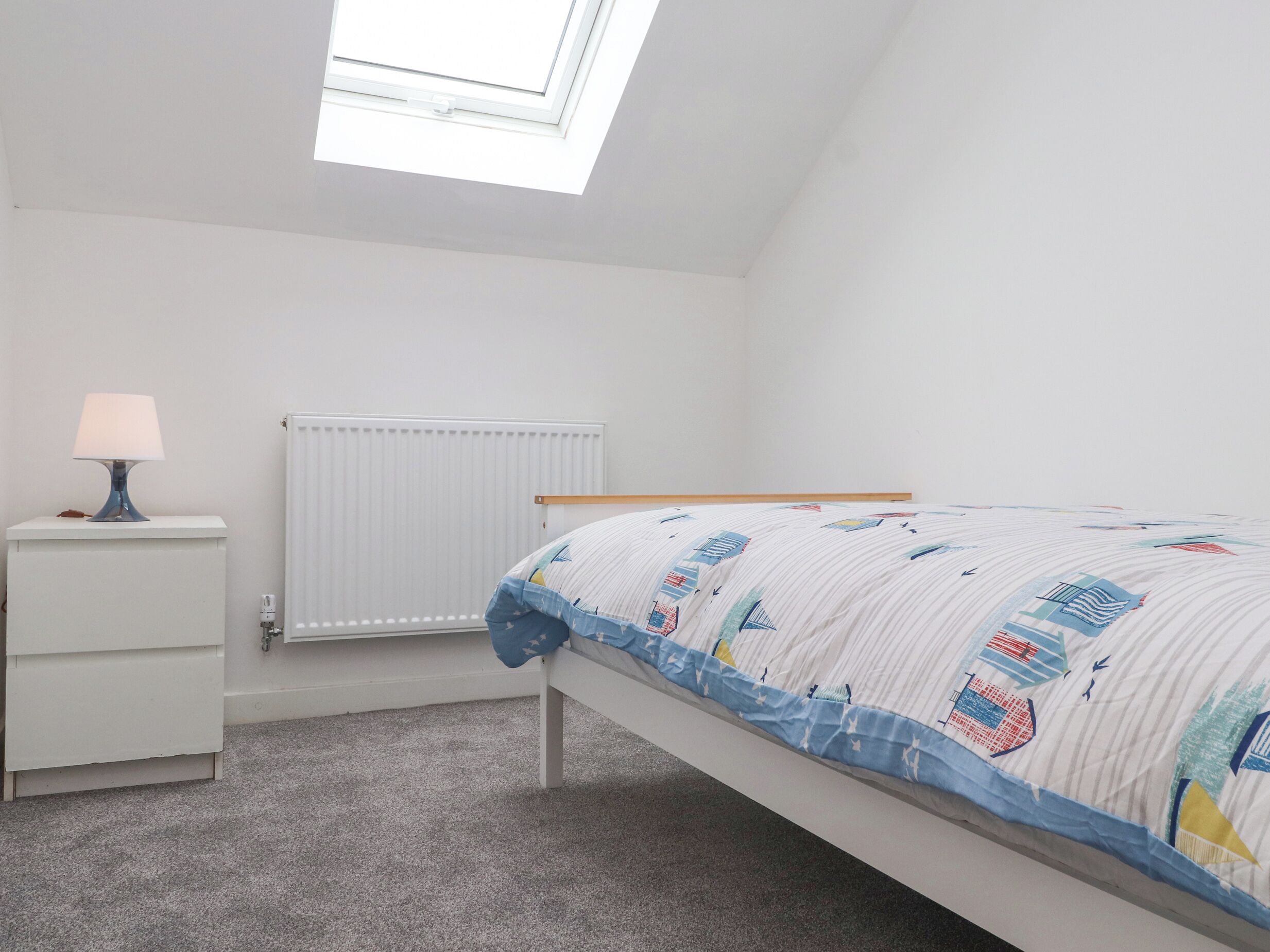 Een slaapkamer met een bed, een nachtkastje met lamp, een radiator en een dakraam.