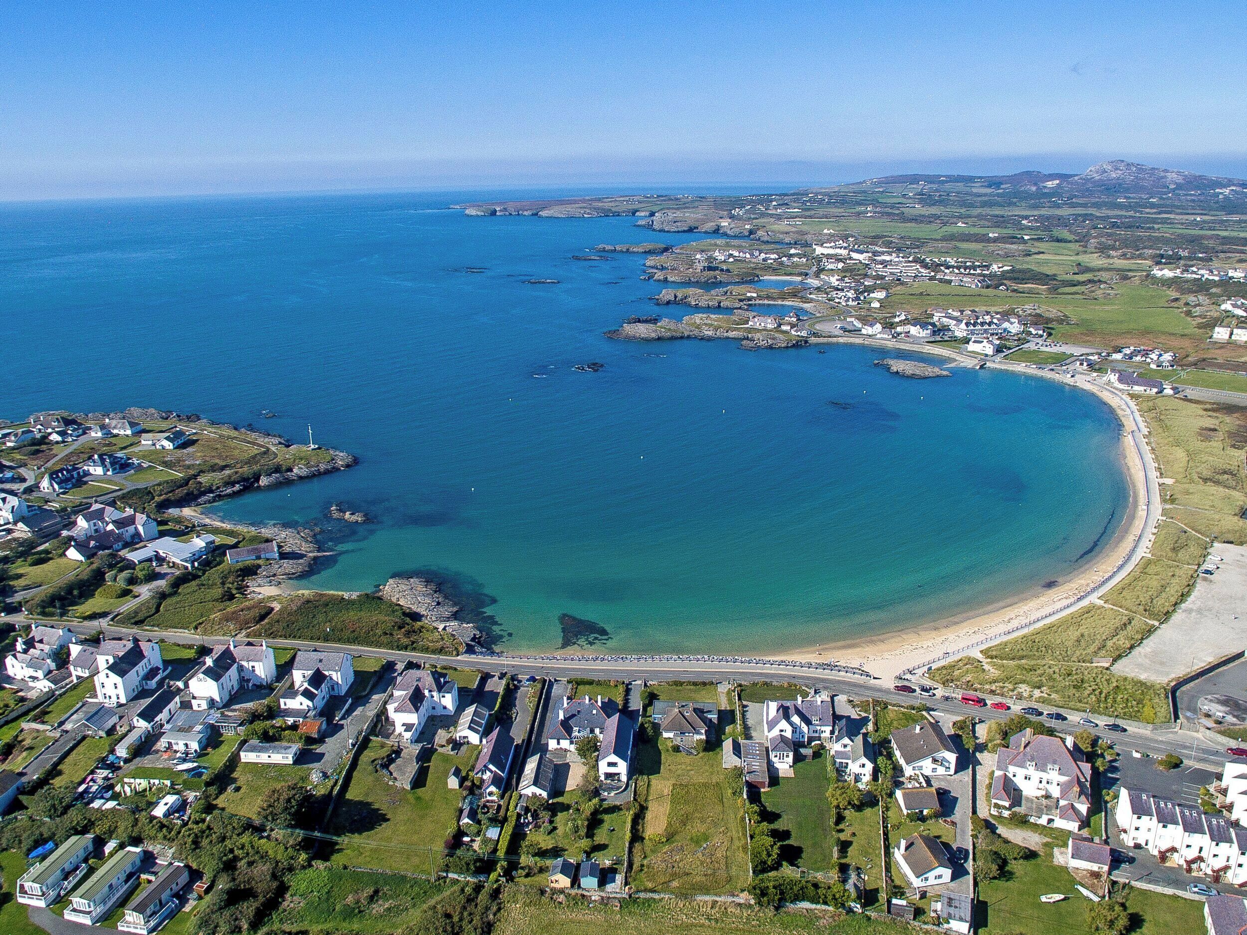 An aerial view of a coastal residential area with houses, a beach, and a clear blue sea.