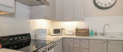 A kitchen with white cabinets, a Smeg stove, a microwave, a toaster, a clock, and a wooden crate labeled "HARDY'S".