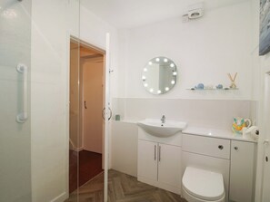 A bathroom with a white sink, a toilet, a mirror with lights, and a shower door.