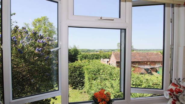 A window with a view of a rural landscape, a potted plant on the windowsill, and a stack of mugs.