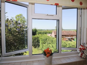 A window with a view of a rural landscape, a potted plant on the windowsill, and a stack of mugs. - Shepherd's Cottage (Bridgnorth)