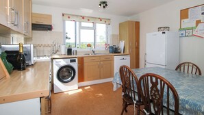 A compact kitchen with a washing machine, a dining table with chairs, and a refrigerator.