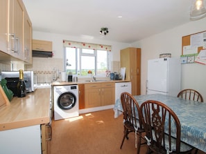 A compact kitchen with a washing machine, a dining table with chairs, and a refrigerator. - Shepherd's Cottage (Bridgnorth)