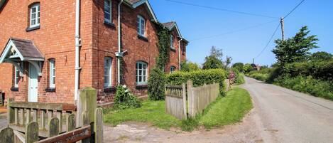A red brick cottage with a wooden gate labeled 'Shepherds Cottage.'