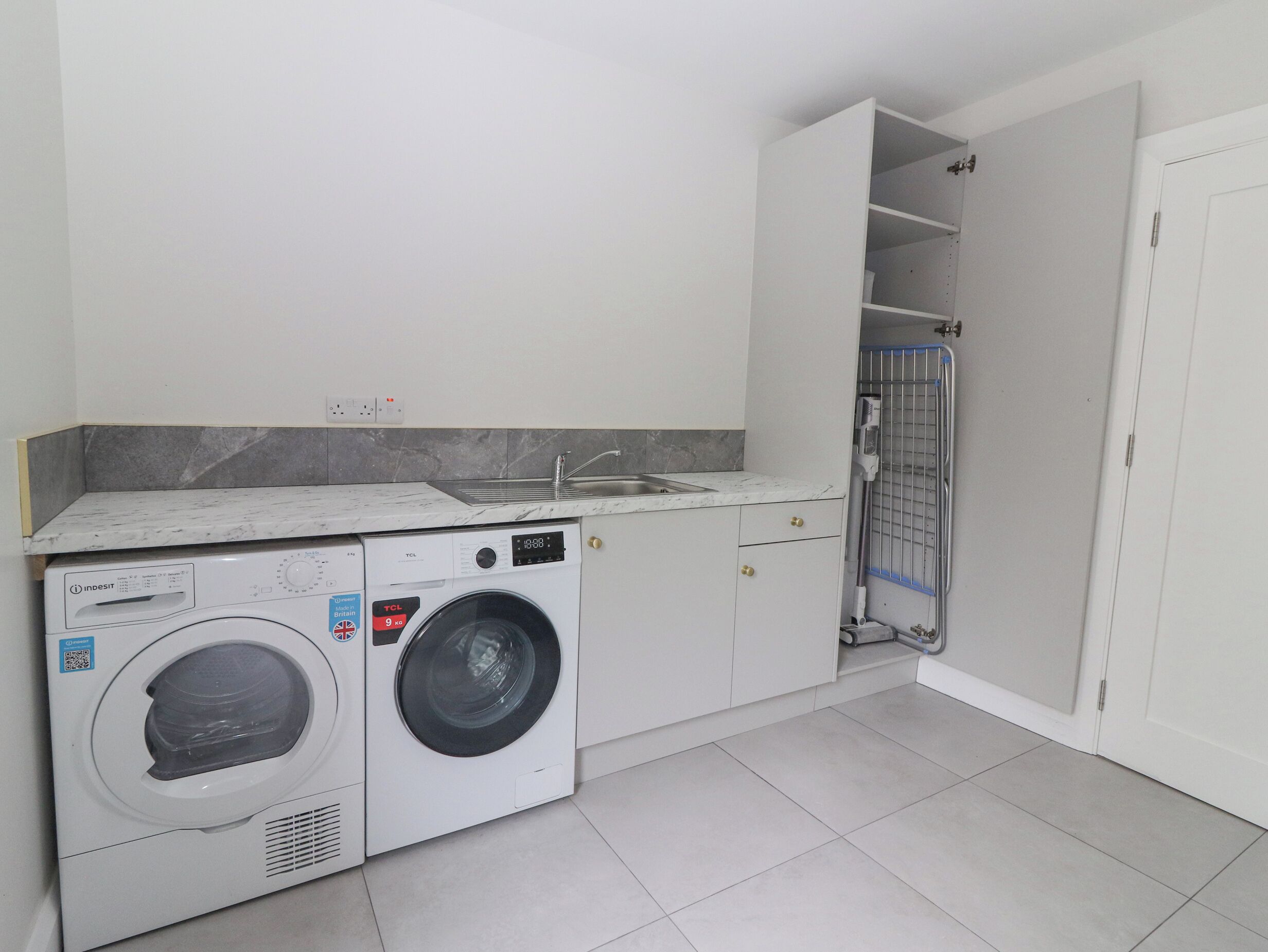Ein kleiner Hauswirtschaftsraum mit Waschmaschine, Trockner, Spüle und Duschkabine.