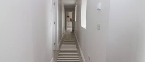 A narrow hallway with a striped rug, white walls, and a door leading to a room.