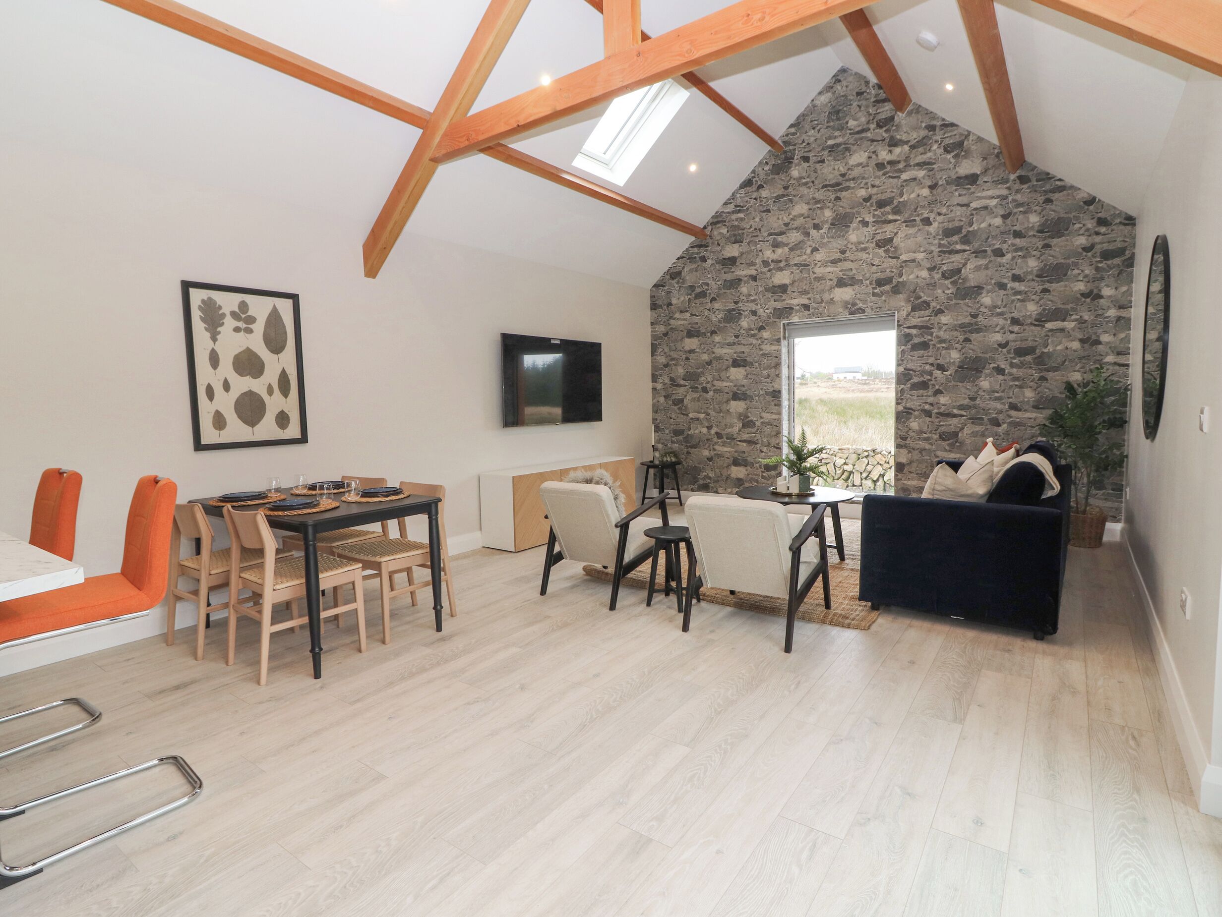 A spacious loft with a stone wall, wooden beams, a dining area, and a cozy seating area with a fireplace.