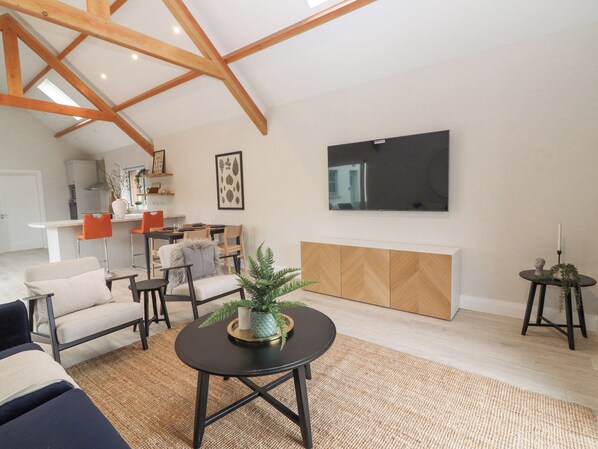 A spacious living room with a high ceiling, a fireplace, a television mounted on the wall, and a dining area with chairs and a table. - Curhoor (Drumkeary)