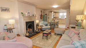 Una sala de estar acogedora con chimenea, asientos cómodos y una cocina al fondo.