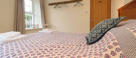 Un dormitorio con cama, ventana con cortinas, puerta de madera y perchero con ganchos.
