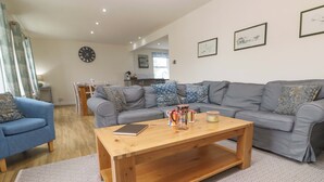 A living room with a grey sofa, a blue armchair, a wooden coffee table, and a patterned rug. - Fair View (Truro)