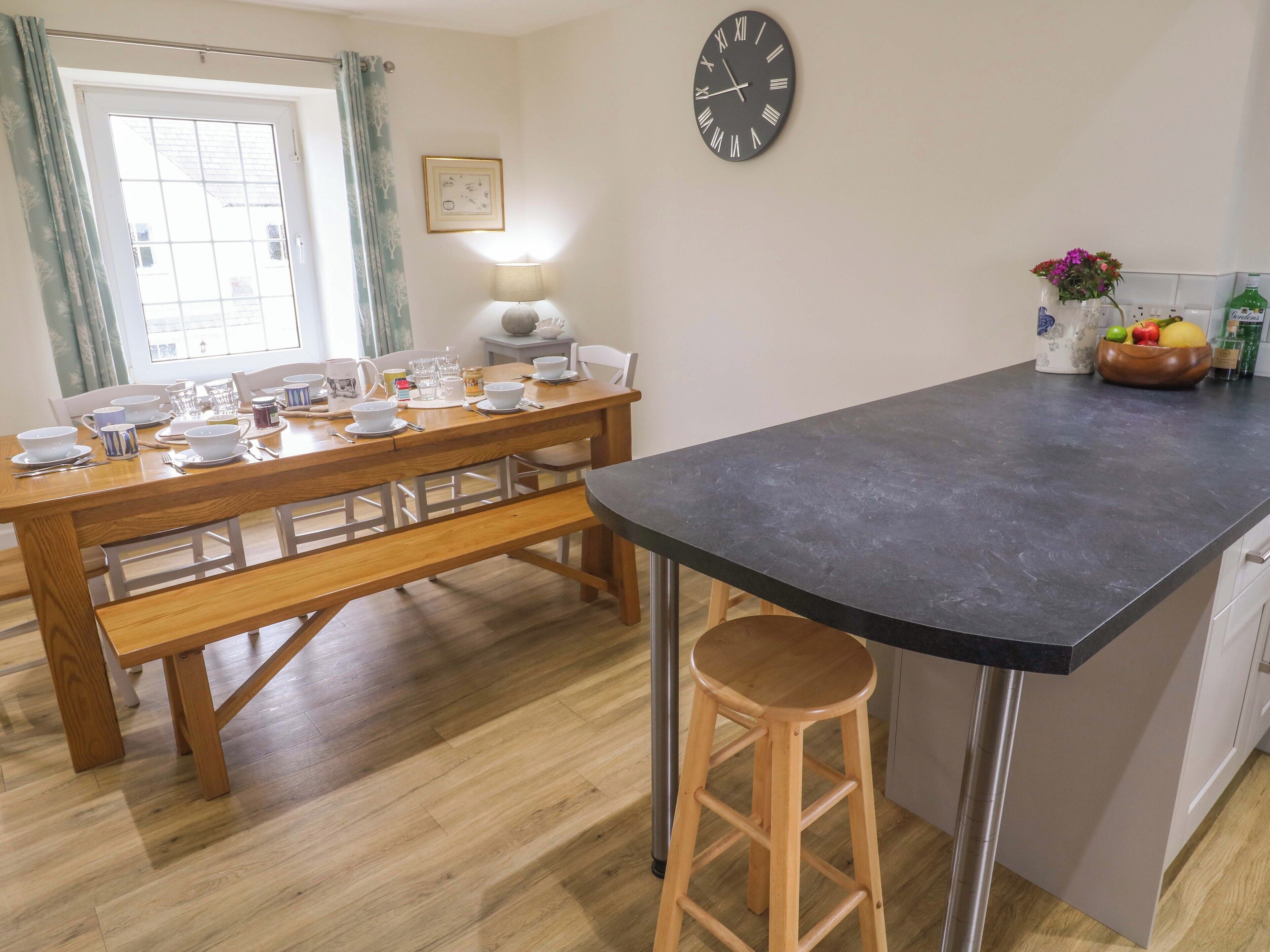 A kitchen with a wooden dining table set for four, a black countertop, and a stool.