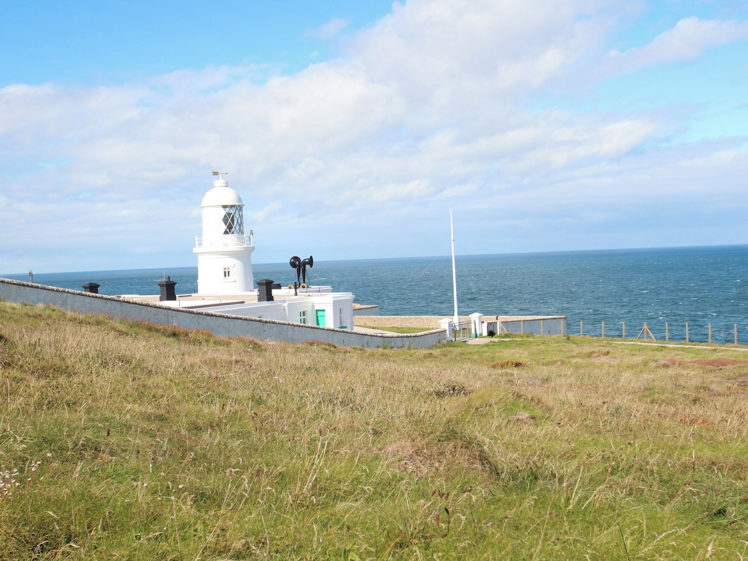 A lighthouse with a white tower and a green door, situated on a grassy cliff overlooking the sea.
