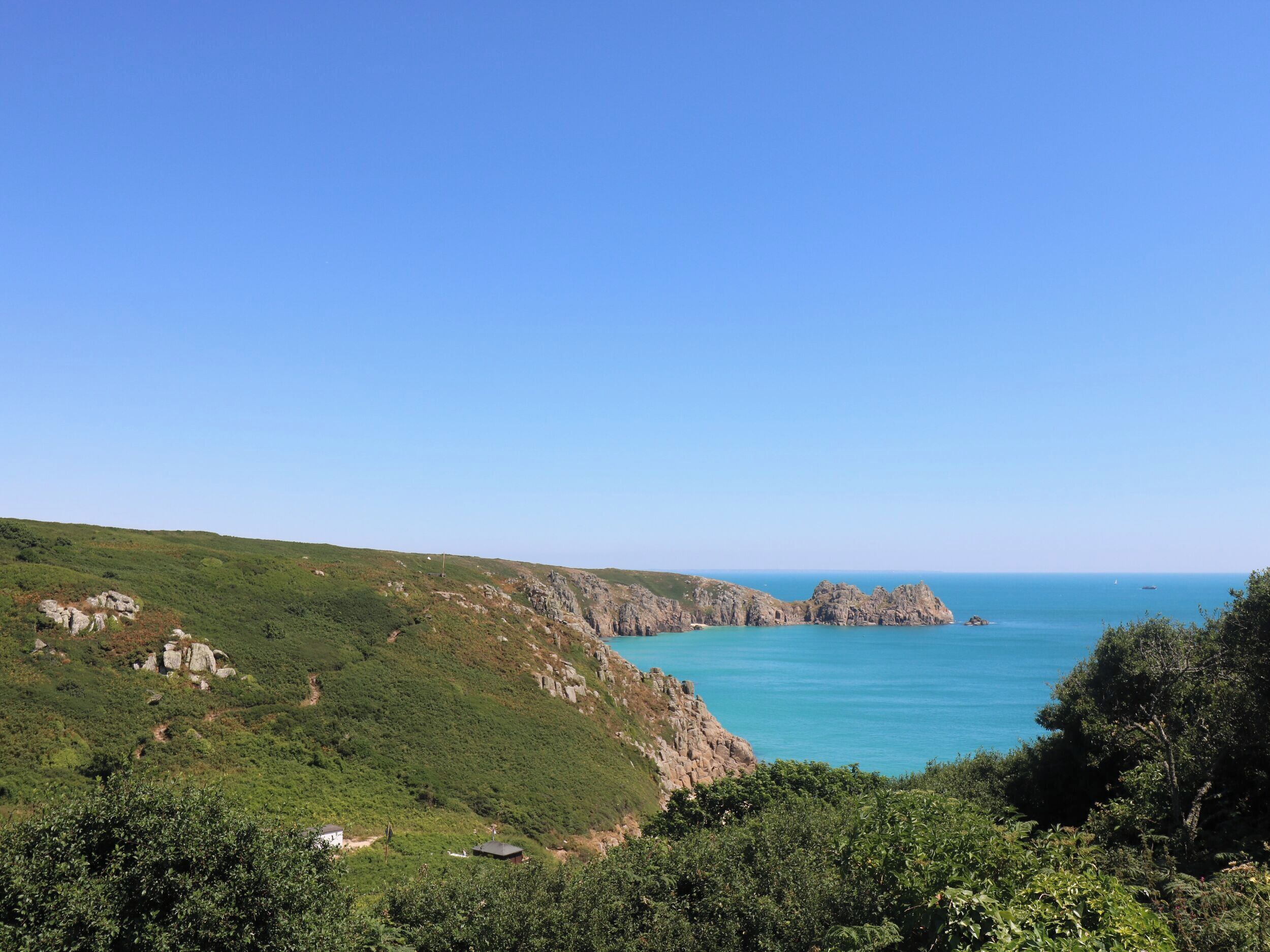 A coastal landscape with a clear sky, rocky cliffs, and a calm sea.