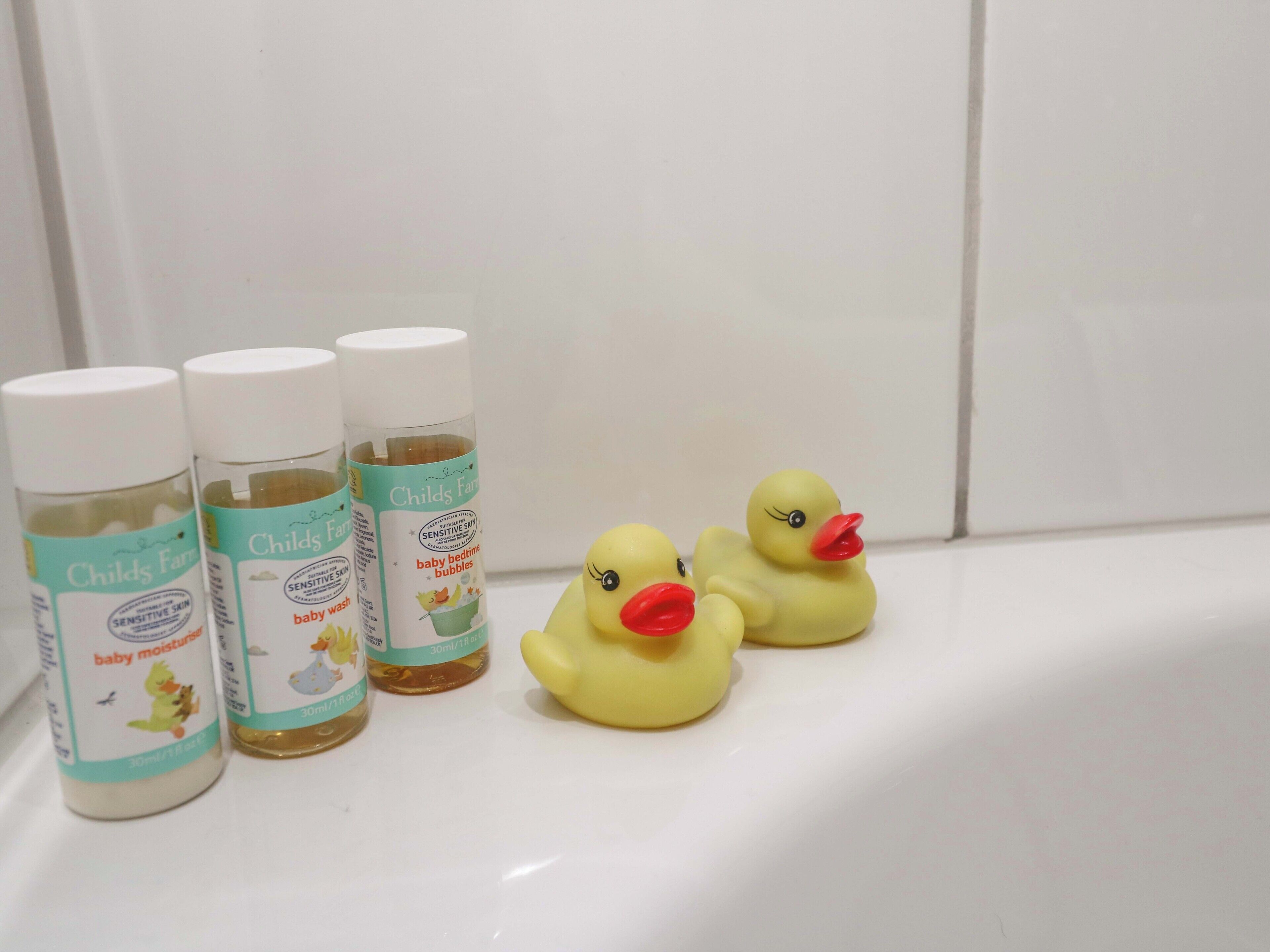 Babyprodukter og to gummibadeænder på en hvid overflade.