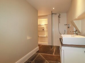 A modern bathroom with a glass shower enclosure, a white sink, and a built-in shelf with towels. - Carew House Cottage (Redruth)