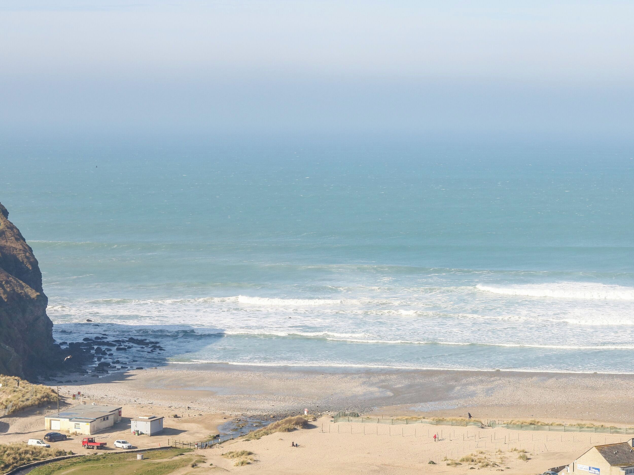 A coastal view with a beach, a cliff, and a few buildings.