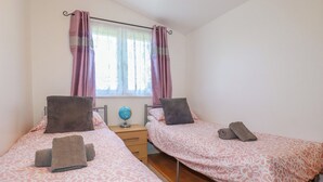Ein Schlafzimmer mit zwei Einzelbetten, jeweils mit einer gemusterten Tagesdecke, Kissen und einem kleinen Nachttisch mit einer Weltkugel.