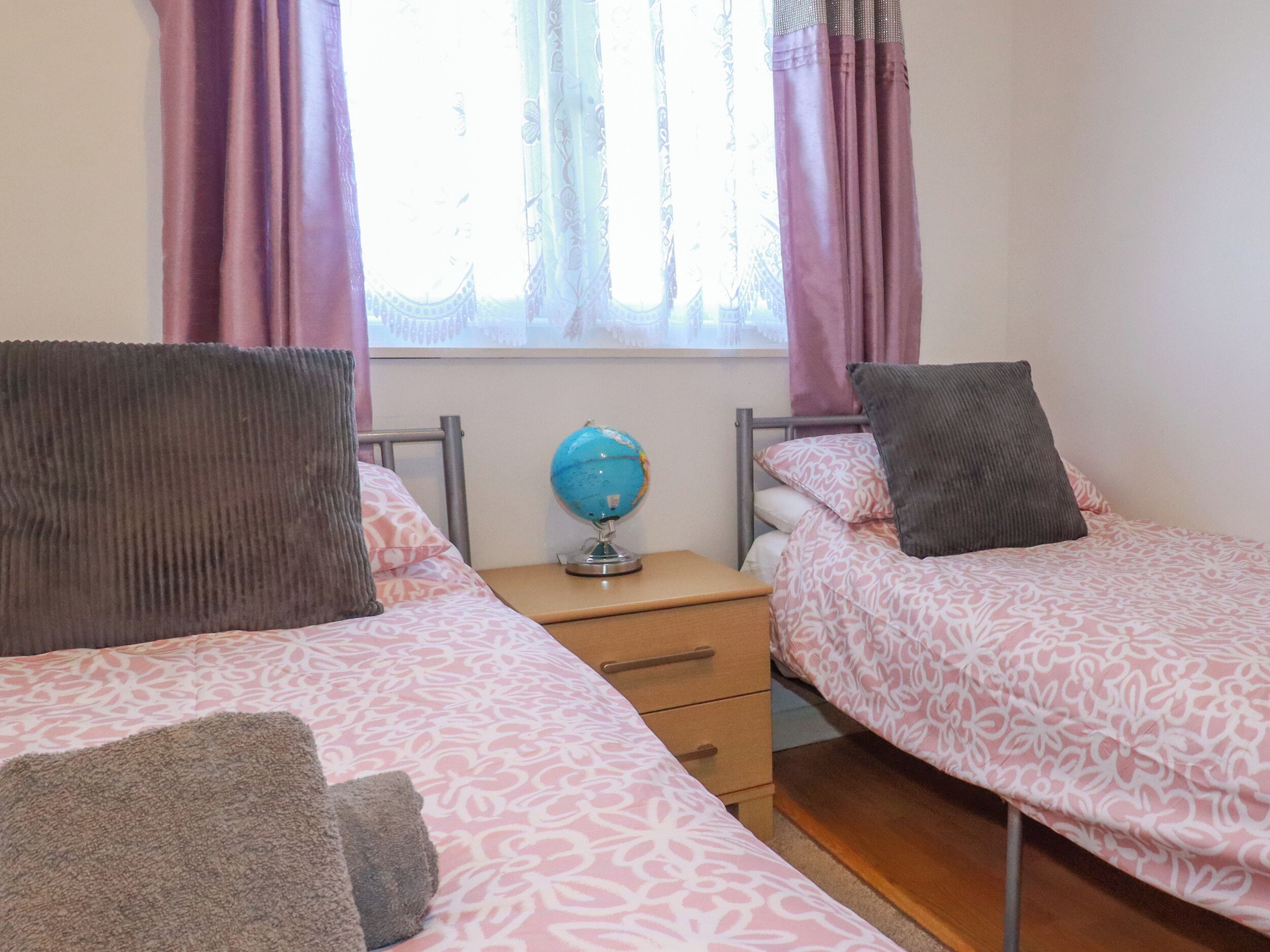 A bedroom with two beds, a nightstand, a globe, and a window with curtains.