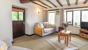 Una sala de estar acogedora con un sofá, una mesa de centro y un mueble para televisor. Hay una puerta y ventanas con cortinas.