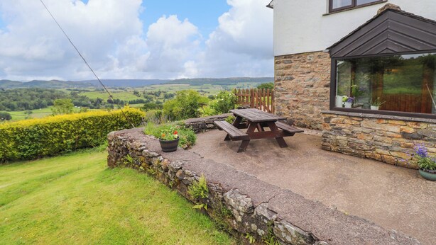 Una casa de piedra con un porche de madera, una mesa de picnic y vistas al campo.