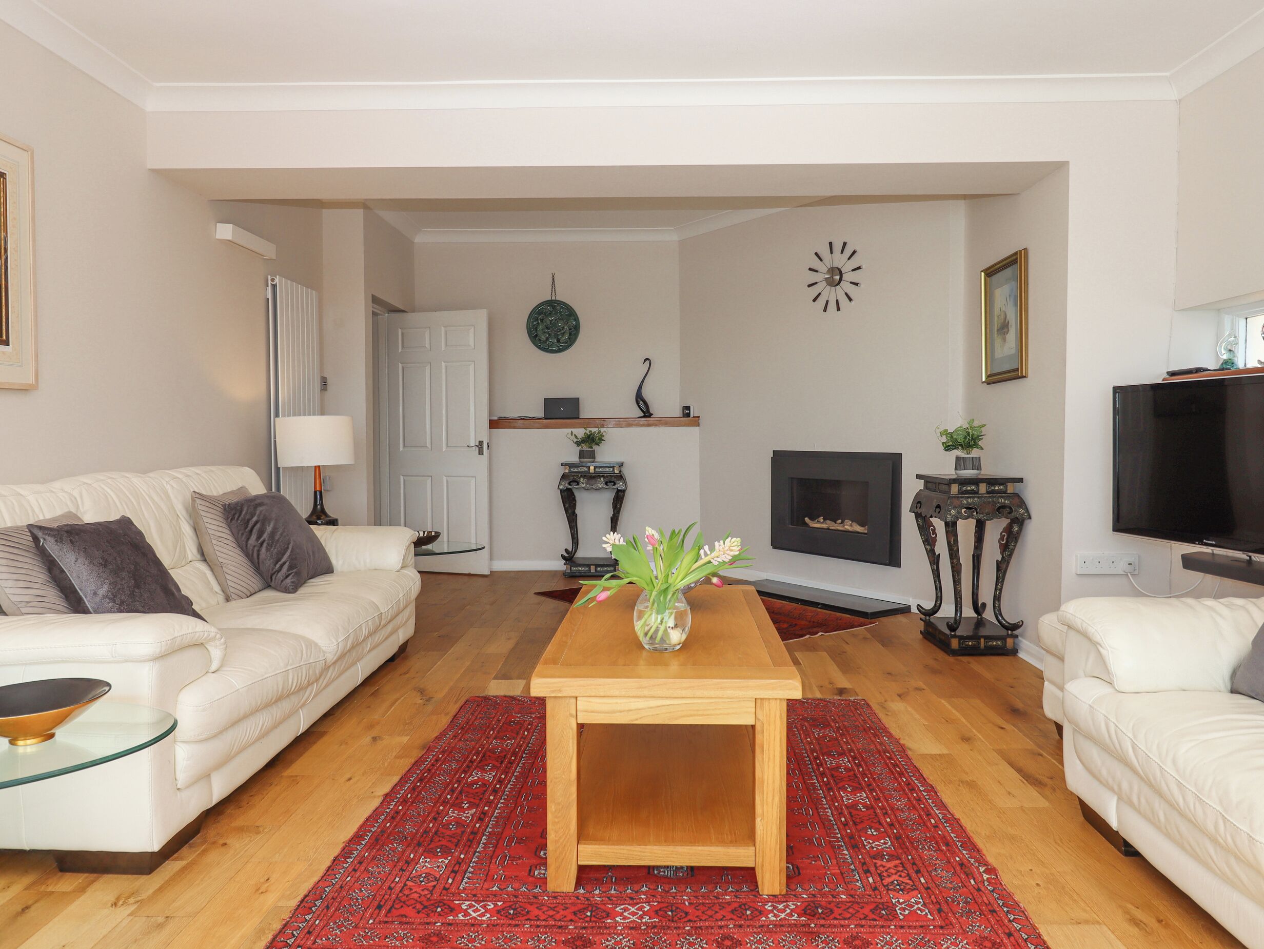 A living room with a white sofa, a wooden coffee table, a red patterned rug, a fireplace, and a television.