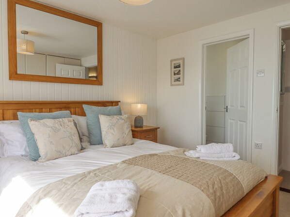 Une chambre à coucher avec un grand lit, une tête de lit en bois, une table de chevet avec une lampe et une porte donnant sur une autre pièce.