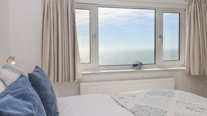 A bedroom with a large window, a bed with blue pillows, and a radiator below the window. - Seahaze (Torpoint)