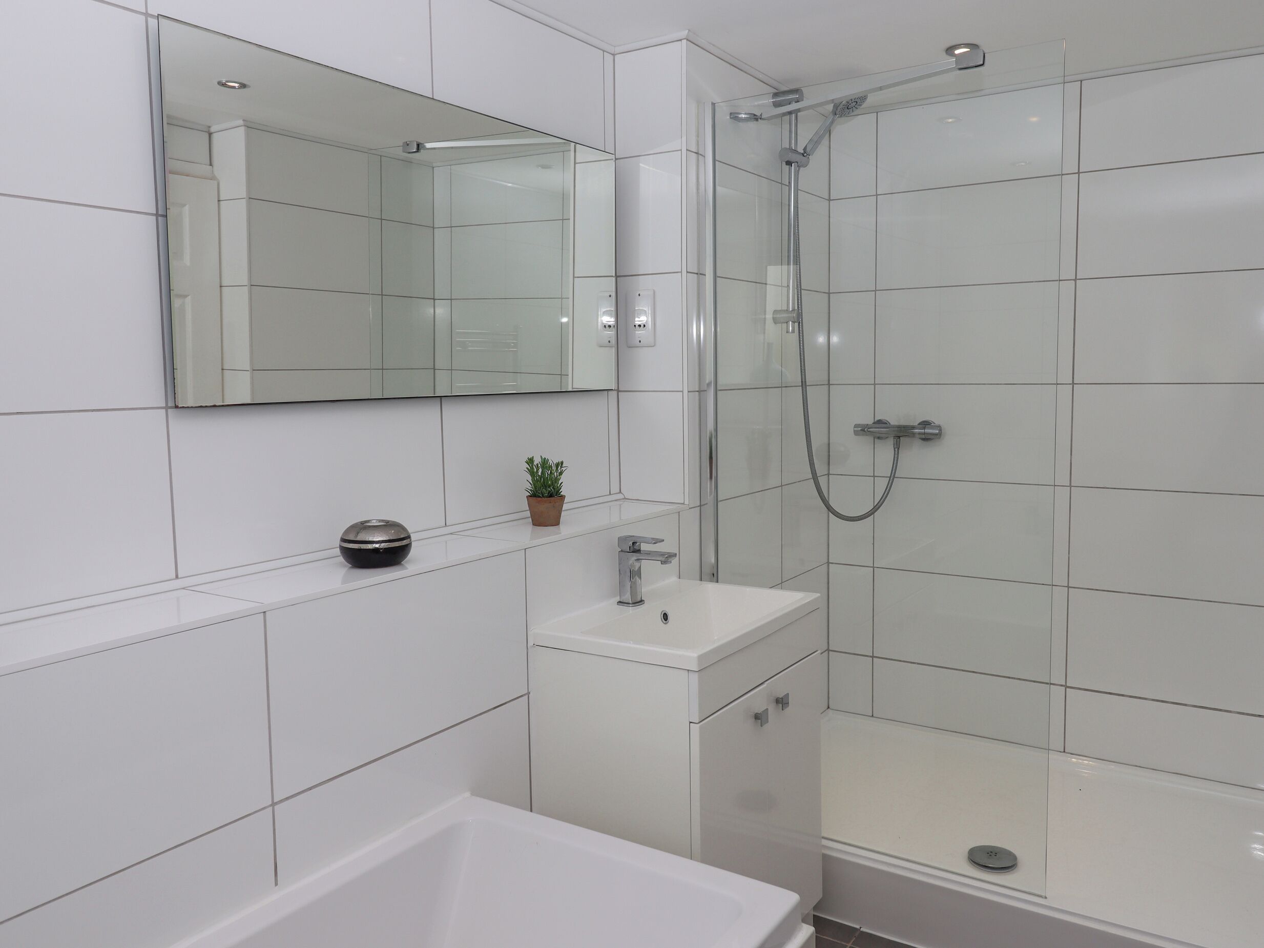 A modern bathroom with a glass-enclosed shower, a white sink, and a mirror above the sink.
