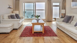 A spacious living room with two white sofas, a wooden coffee table, and a red rug. Large windows offer a view of the sea. - Seahaze (Torpoint)