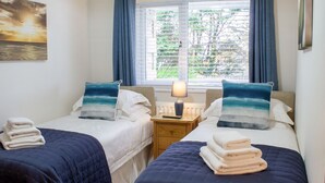 Een hotelkamer met twee bedden, elk voorzien van een blauw-wit kussen, een nachtkastje met een lamp, en uitzicht op groen door het raam.