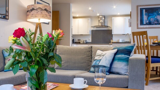 Een woonkamer met een bank, een salontafel, een vaas met bloemen en een glas water.
