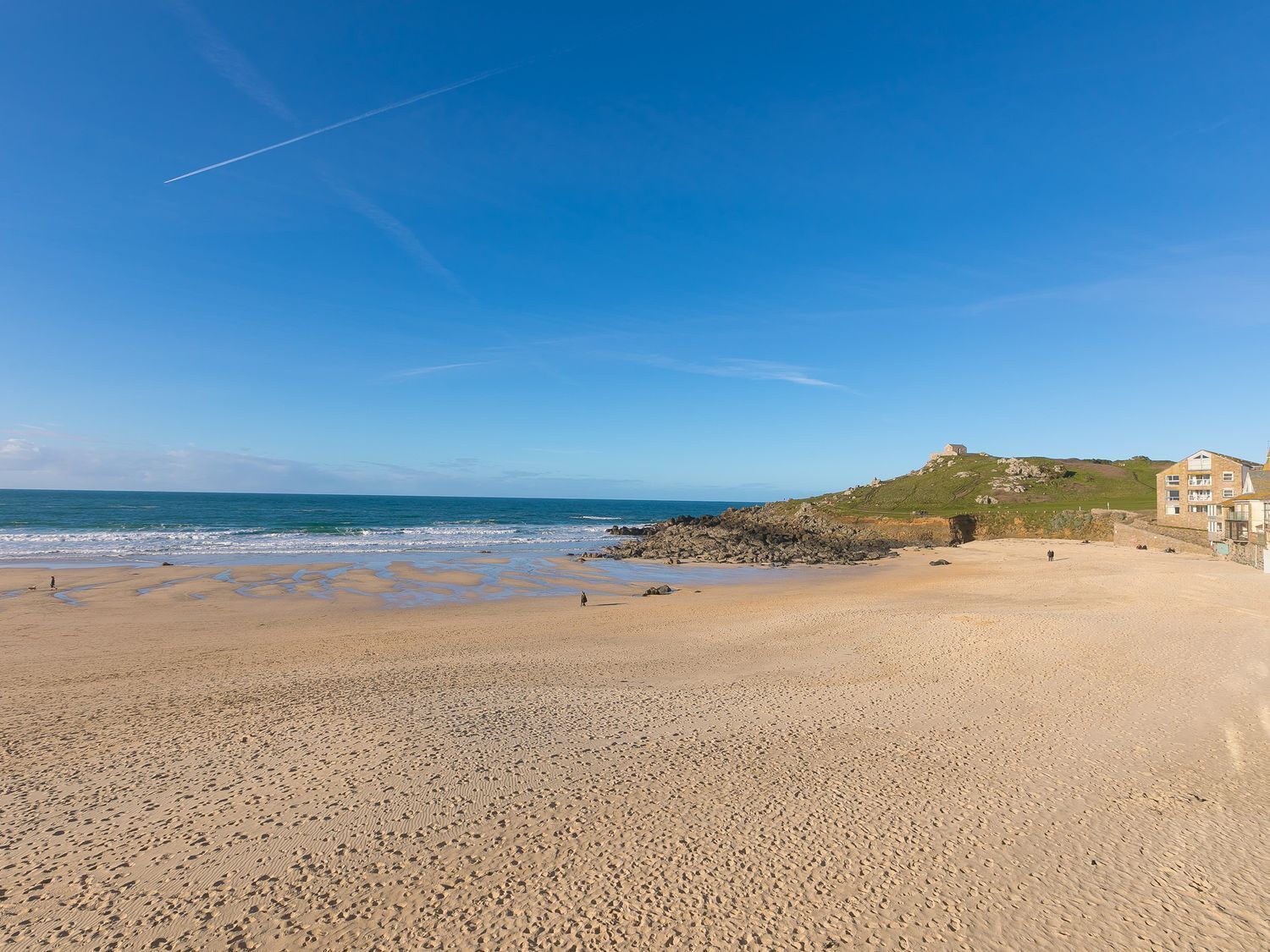 A beach with a rocky shoreline, a clear blue sky, and a building with multiple windows.